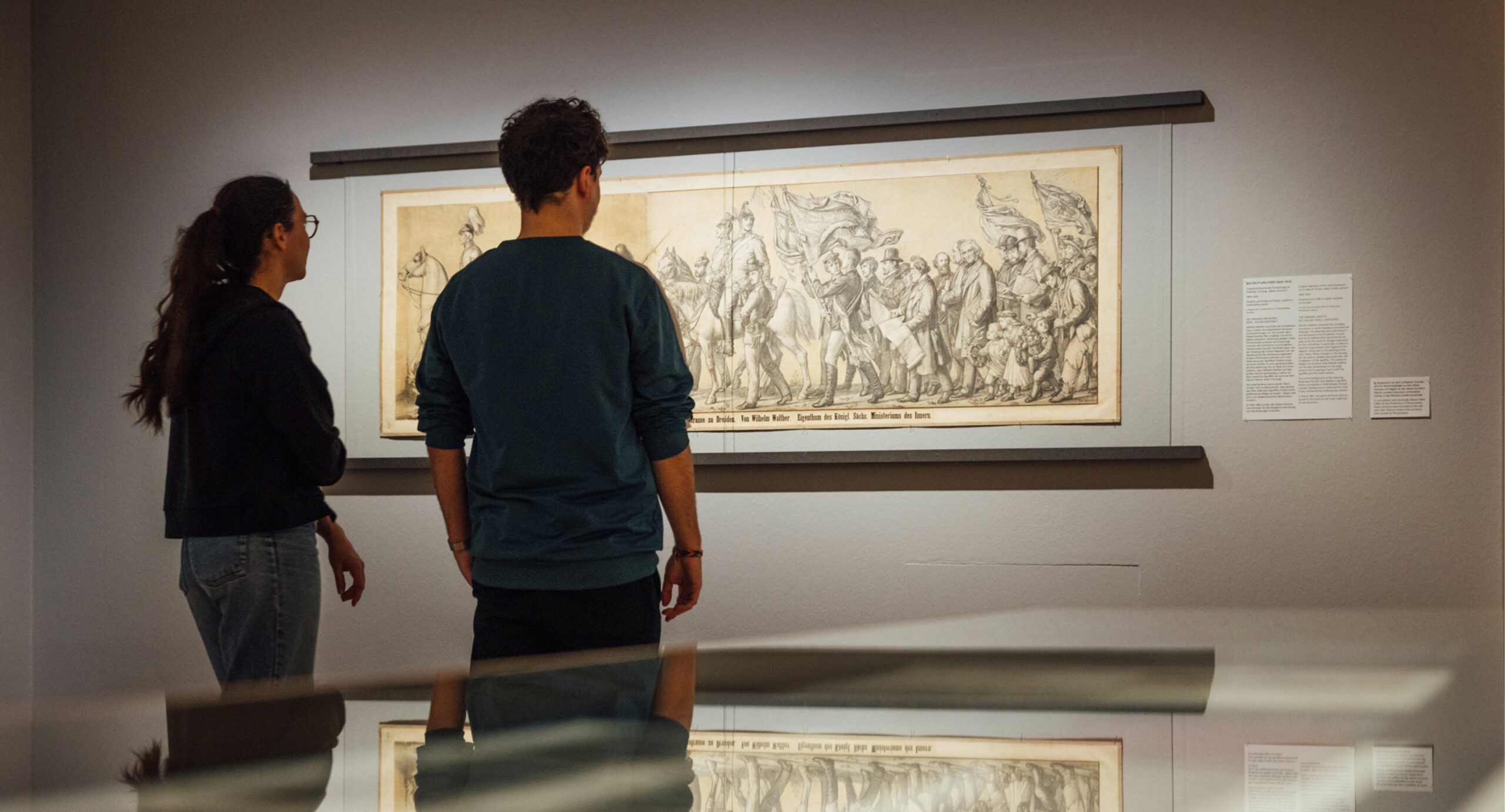 Zu sehen sind zwei Personen in Rückenansicht vor einer Grafik im Ausstellungsraum.