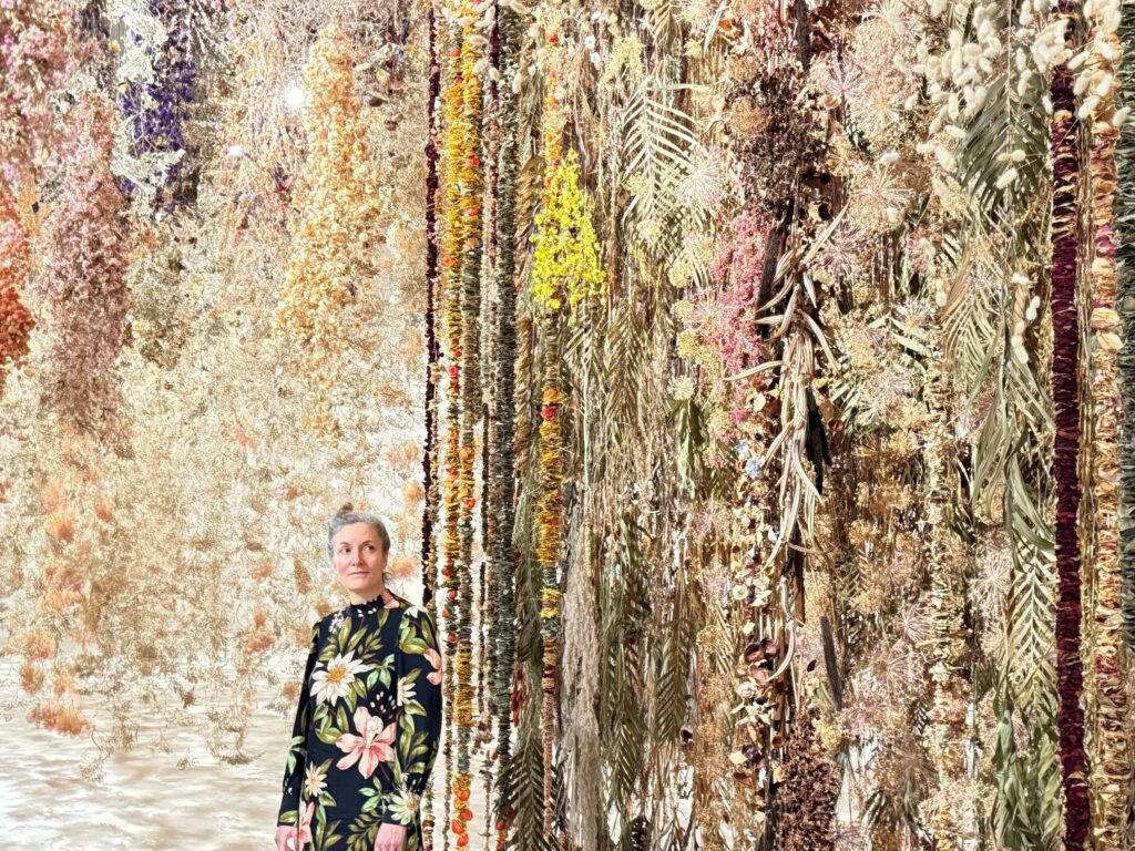 Zu sehen ist die Künstlerin in einem Blumenkleid vor ihrer Installation.