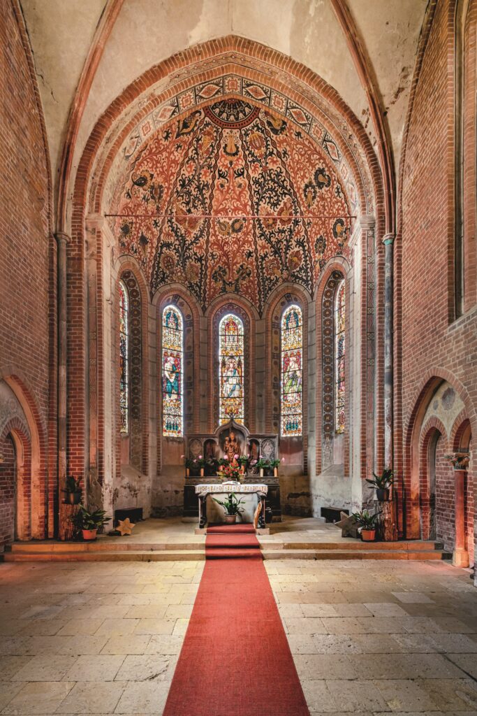 Man sieht das Kircheninnere mit dem Blick in Richtung des Chorraums, zu dem ein roter Teppich führt.
