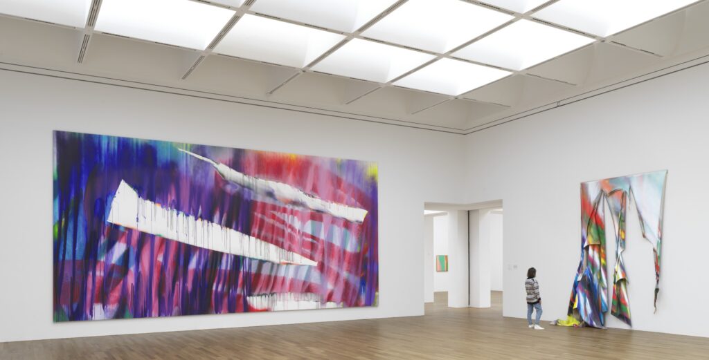 Zu sehen ist ein Ausstellungsraum mit einer Besucherin vor einer Installation Katharina Grosses.